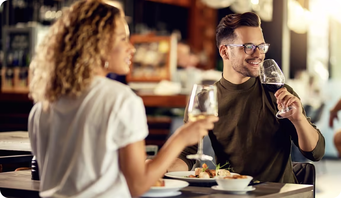 A smiling couple enjoys a restaurant meal with glasses of wine.