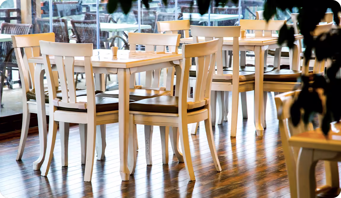 An empty dining room with wooden flooring, white-framed tables and chairs with dark brown seats.